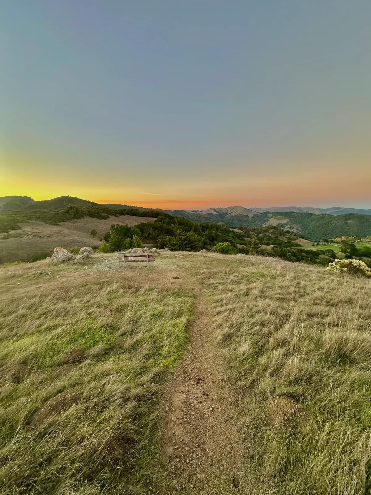 Dirt trail crossing a grassy hilltop toward rolling hills at sunset