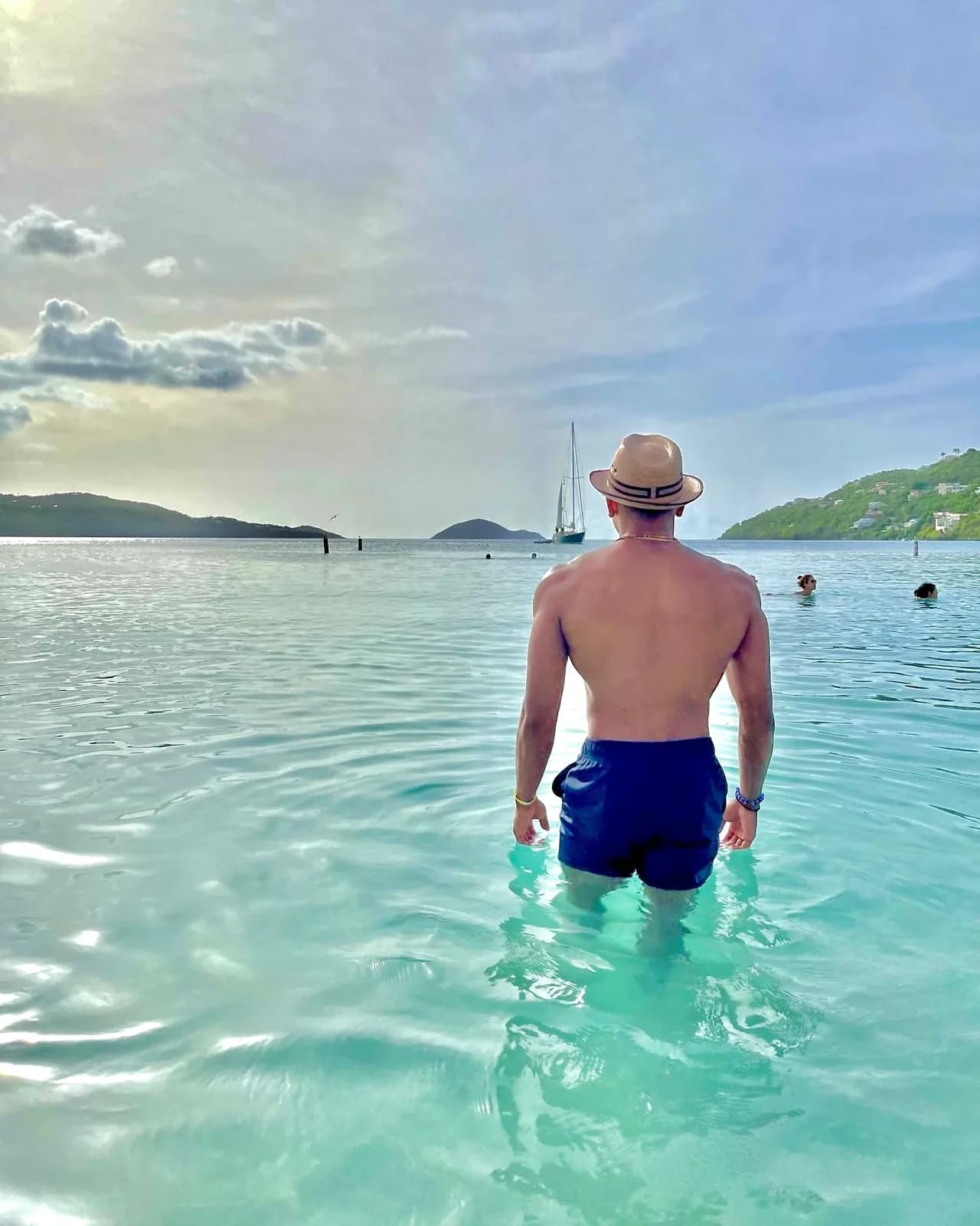 Wading into a calm turquoise bay toward a sailboat at golden hour